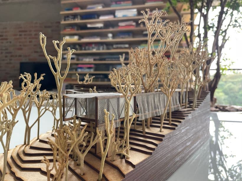 Maquete da Casa Matutu com estrutura de madeira e telas metálicas entre árvores